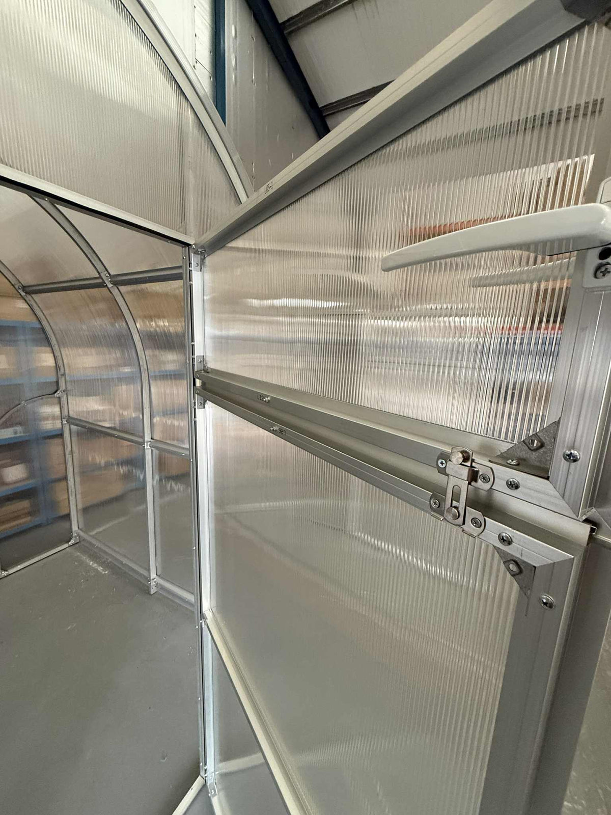 Partial view of a Sigma 200 (Gen III) greenhouse with transparent panels and metal frame.