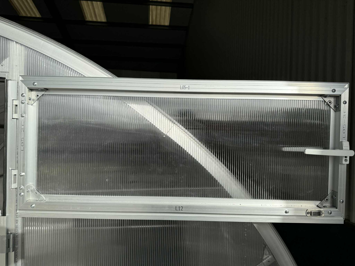 Metallic window of a Sigma 300 (Gen III) greenhouse with visible branding on a dark background