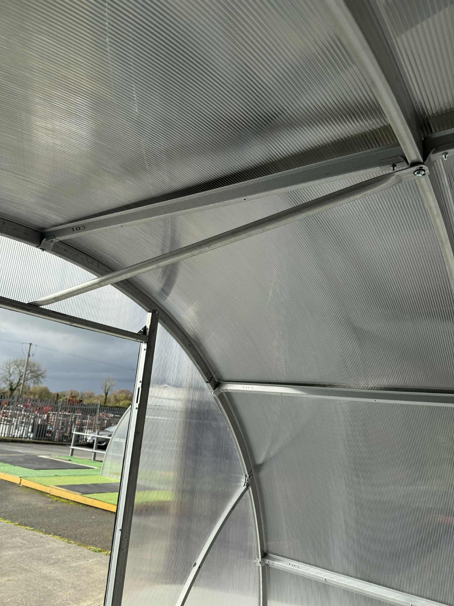 Metallic canopy structure of a  Sigma 300 (Gen III) greenhouse with a view of a sports field in the background