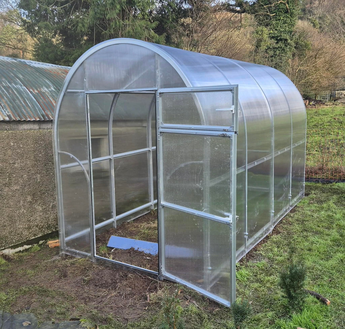 Sigma 2x8 (Gen III) greenhouse with a curved glass roof and walls on a grassy area.