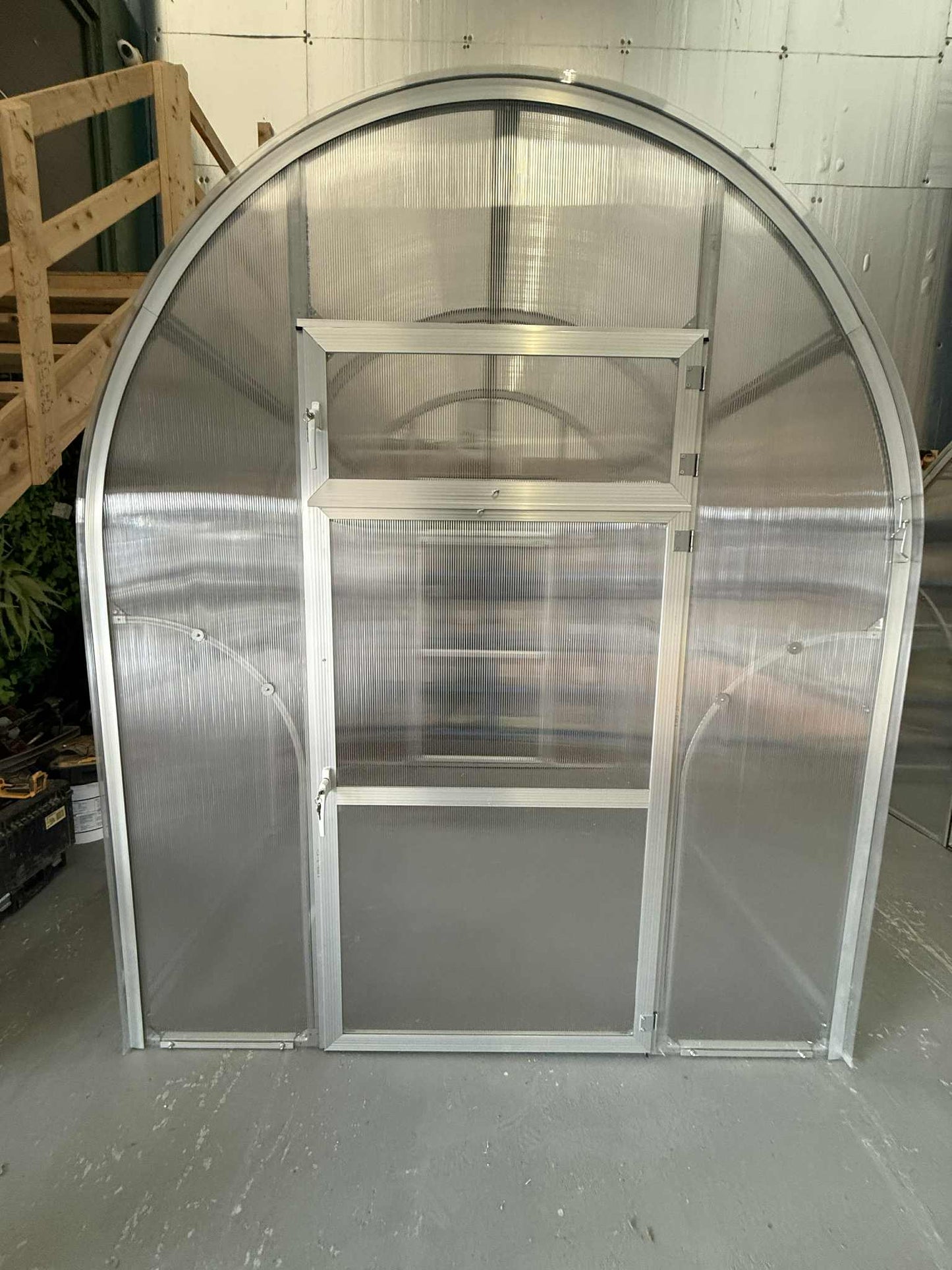 Metal Sigma 200 (Gen III) greenhouse structure with curved roof and transparent panels on a concrete floor.